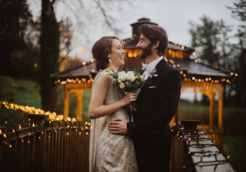 A couple embraces on a bridge decorated with fairy lights at Fernhill House Hotel.