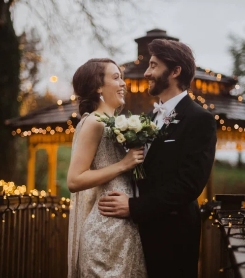 A couple embraces on a bridge decorated with fairy lights at Fernhill House Hotel.