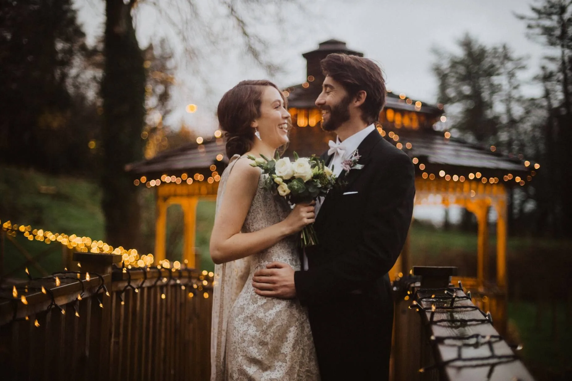 A couple embraces on a bridge decorated with fairy lights at Fernhill House Hotel.