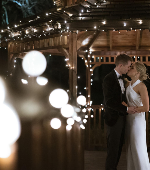 A couple kisses under a fairy-lit gazebo at Fernhill House Hotel, creating a romantic evening atmosphere.