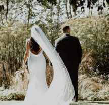 Couple walking in lush garden at Fernhill House Hotel, bride's veil flowing elegantly.