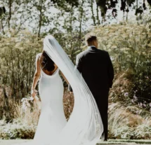 A couple in wedding attire strolls through lush gardens at Fernhill House Hotel.