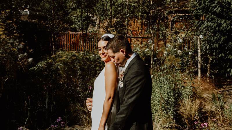 A couple embraces in a lush garden at Fernhill House Hotel.