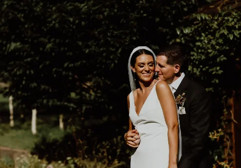 A joyful couple embraces in a lush garden at Fernhill House Hotel, surrounded by greenery.