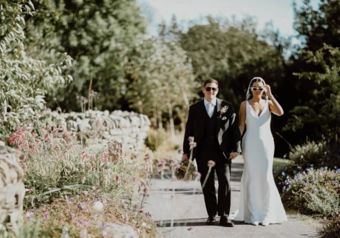 A joyful couple walks hand in hand through a lush garden at Fernhill House Hotel.