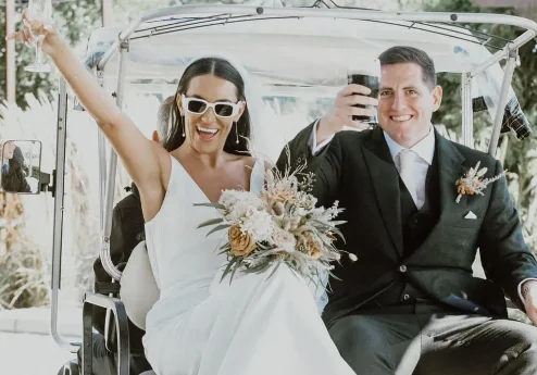 A joyful couple in a wedding attire toasting on a golf cart at Fernhill House Hotel.