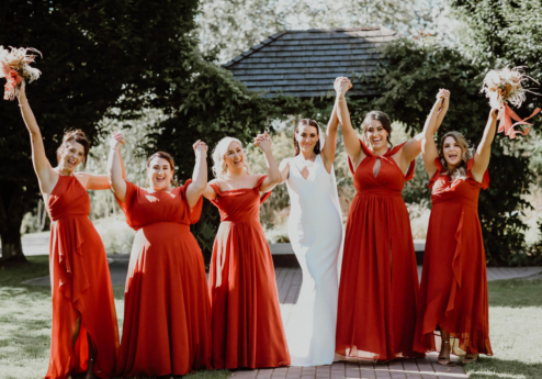 A joyful bridal party celebrates outdoors, holding bouquets at Fernhill House Hotel garden.