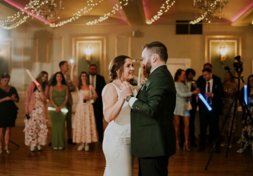 A couple shares a dance in a warmly lit ballroom during a joyful wedding celebration.