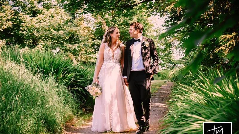 Couple walking through lush garden path, smiling on a sunny day at Fernhill House Hotel.