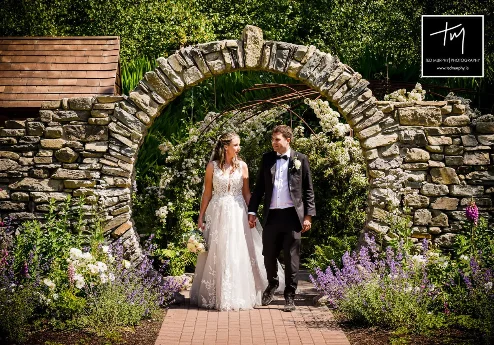 A couple walks hand in hand through a floral arch at Fernhill House Hotel garden.