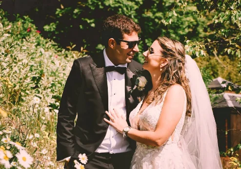 A joyful couple embraces in a garden, surrounded by daisies under the warm sun.