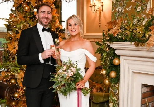 A couple in formal attire toast with champagne by a Christmas tree at Fernhill House Hotel.