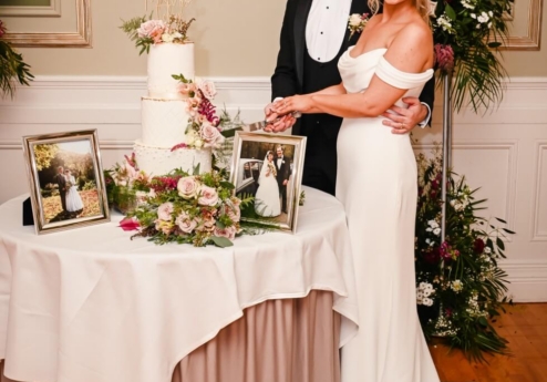Couple cutting wedding cake at Fernhill House Hotel with family photos on table.