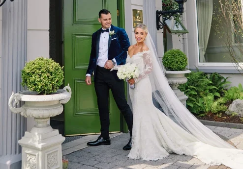 A couple in wedding attire stands by Fernhill House Hotel entrance.