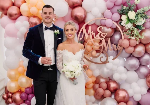 A joyful couple at a wedding, posing in front of a balloon arch with "Mr & Mrs" sign.