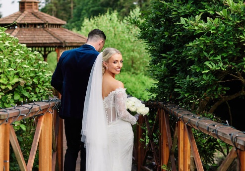 Bride and groom walking on rustic bridge at Fernhill House Hotel gardens.