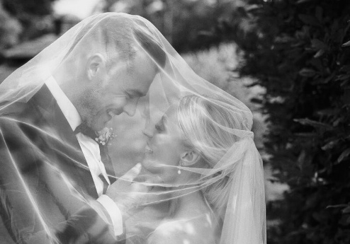 A joyful couple shares a tender moment under a wedding veil at Fernhill House Hotel garden.
