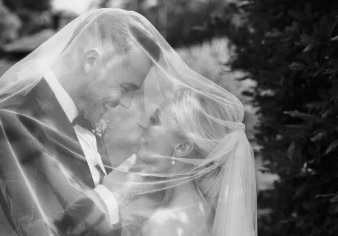 A couple embraces under a veil at Fernhill House Hotel garden.