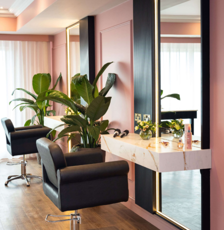Elegant salon area with plush chairs, large mirrors, and vibrant greenery.