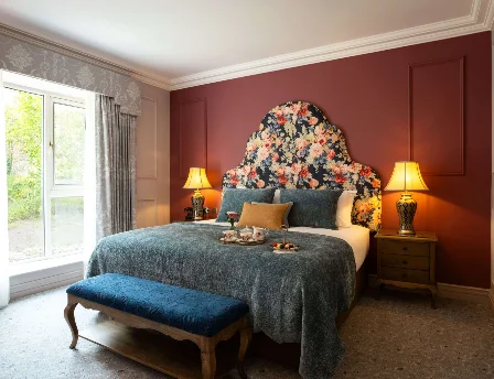 Elegant hotel room with floral headboard and sunlight through window, creating a cosy ambience.