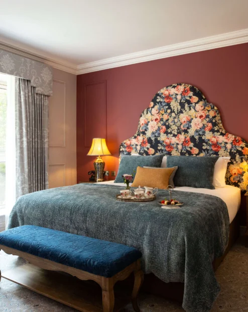 Elegant hotel room with floral headboard and sunlight through window, creating a cosy ambience.