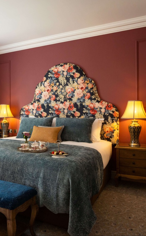 Cosy hotel room with large bed, floral headboard, and tray of refreshments.