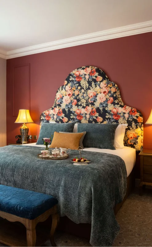 Elegant hotel room with floral headboard and sunlight through window, creating a cosy ambience.