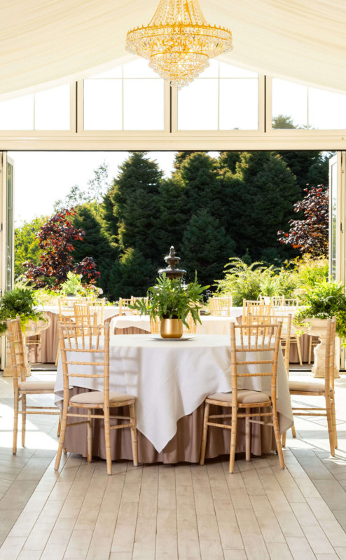 Elegant dining area in a sunlit conservatory with lush garden views.