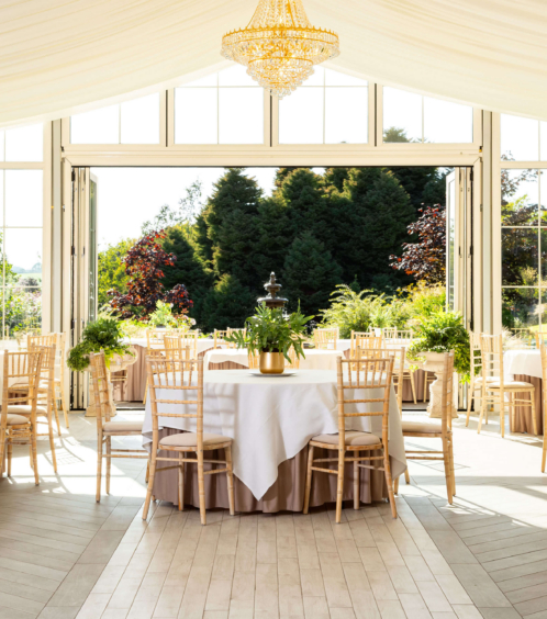 Elegant dining area in a sunlit conservatory with lush garden views.
