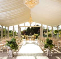 Elegant wedding setup in a bright, sunlit garden marquee with ornate chandeliers.