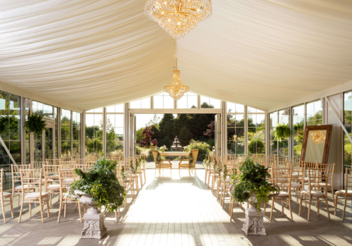 Elegant wedding setup in a bright, sunlit garden marquee with ornate chandeliers.