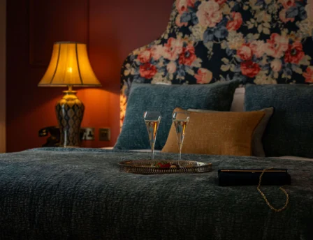 Cosy hotel room with floral decor and champagne on the bed.