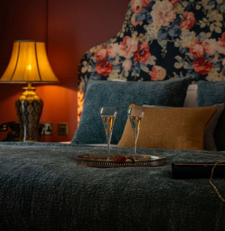 Cosy hotel room with floral decor and champagne on the bed.