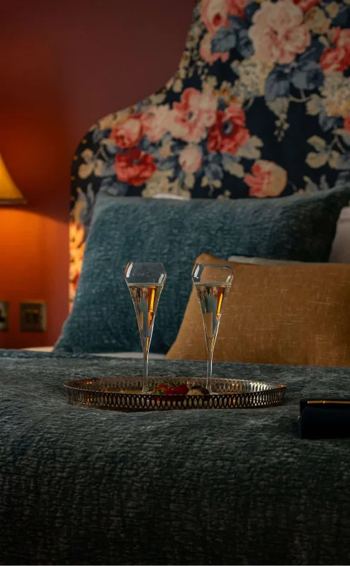 Cosy hotel room with floral decor and champagne on the bed.