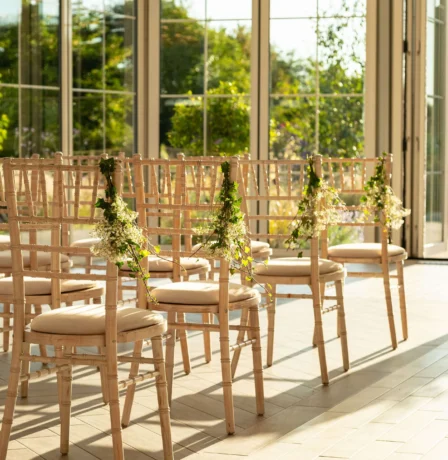Sunlit wedding ceremony setup with elegant chairs in Fernhill House Hotel's garden room.