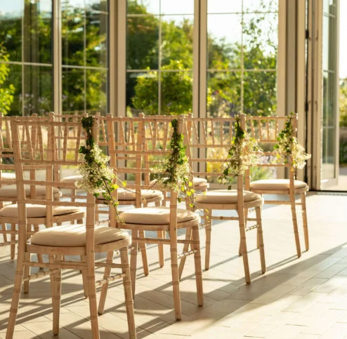 Sunlit wedding ceremony setup with elegant chairs in Fernhill House Hotel's garden room.