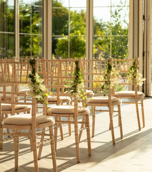 Sunlit wedding ceremony setup with elegant chairs in Fernhill House Hotel's garden room.