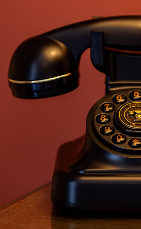 Cosy hotel room with vintage black rotary phone on wooden table, warm lighting.
