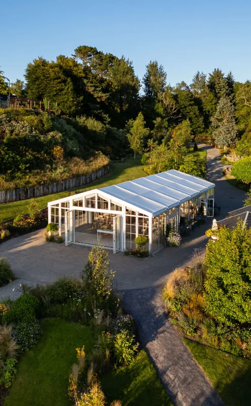 A serene garden setting with a glasshouse under clear blue skies at Fernhill House Hotel.