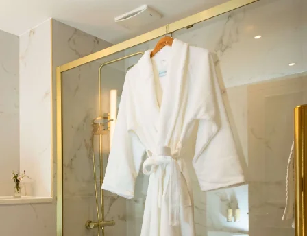 Elegant hotel bathroom with robe hanging in marble shower.
