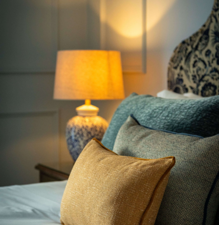 Cosy hotel room with soft lighting and elegant decor, featuring plush cushions on a bed.