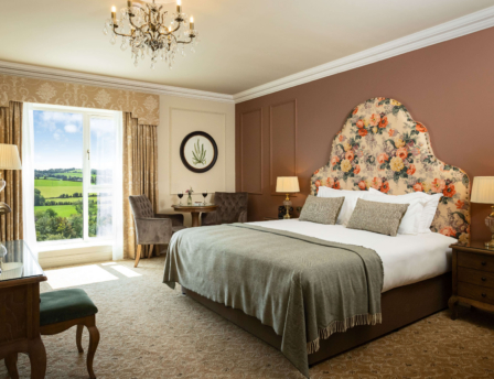 Elegant hotel room with countryside view, plush king-size bed, and cosy seating area.