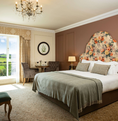 Elegant hotel room with countryside view, plush king-size bed, and cosy seating area.