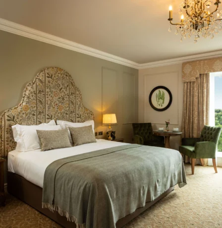 Elegant hotel room with a plush bed, green accents, and a view of lush gardens.