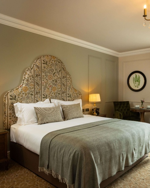 Elegant hotel room with a king-sized bed, green chairs, and a scenic view of lush greenery.