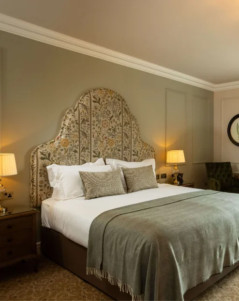 Elegant hotel room with a plush bed, green accents, and a view of lush gardens.