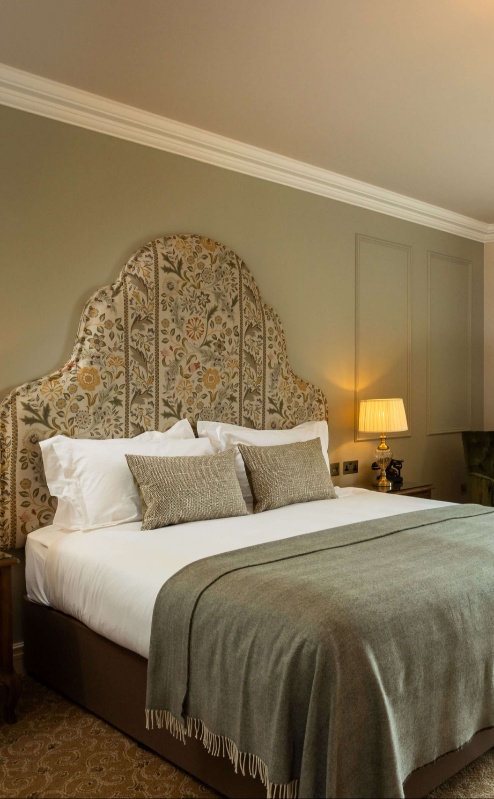 Elegant hotel room with a king-sized bed, green chairs, and a scenic view of lush greenery.