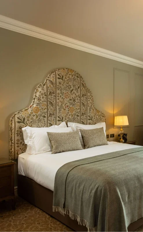 Elegant hotel room with a plush bed, green accents, and a view of lush gardens.