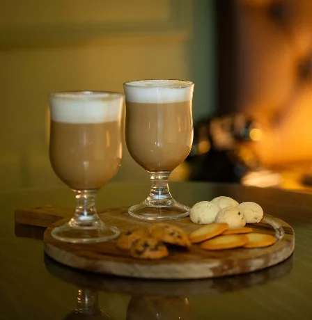 Warm drinks and biscuits on a wooden tray in a cosy hotel room setting.