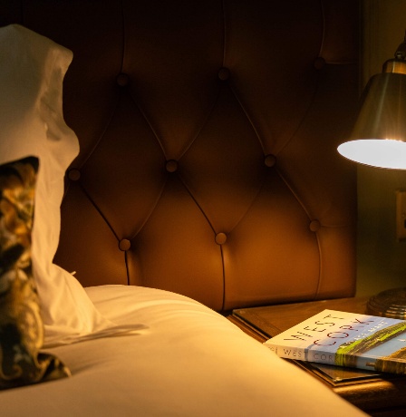 Cosy hotel room with a lamp and books on a bedside table.